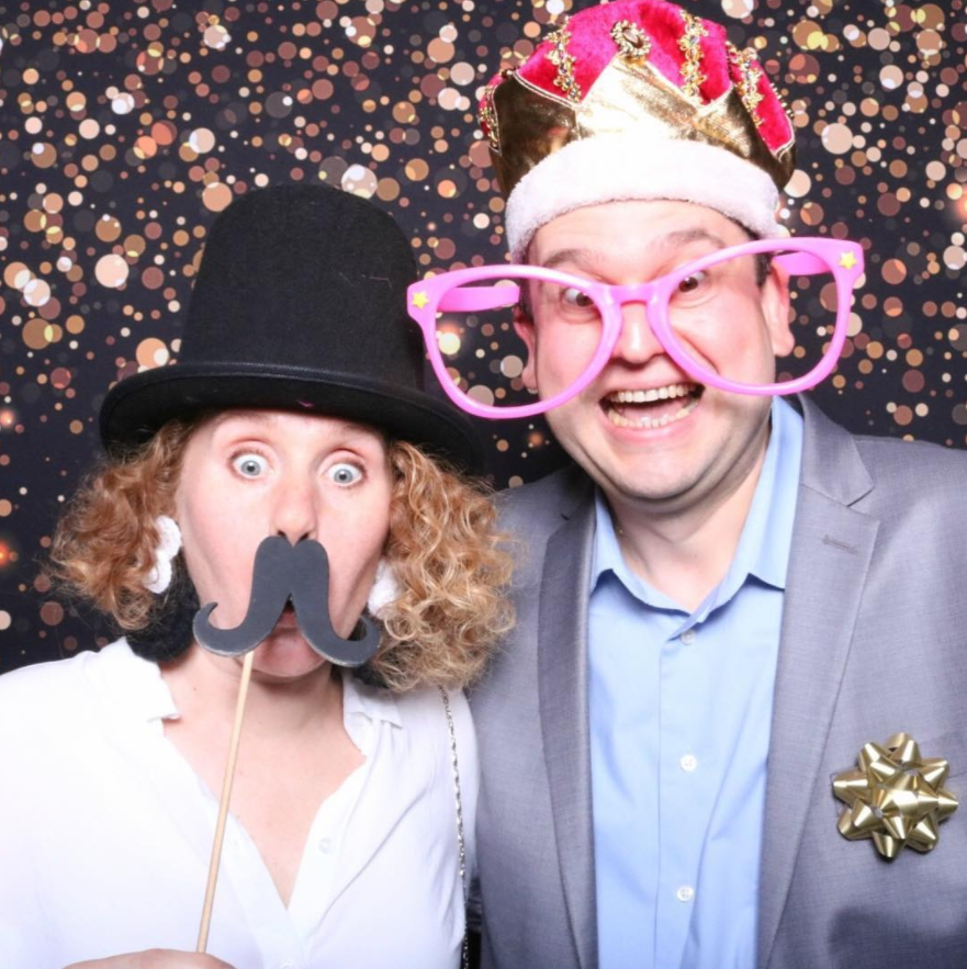 A man and a woman taking a selfie picture. A glitter backdrop is in the background.