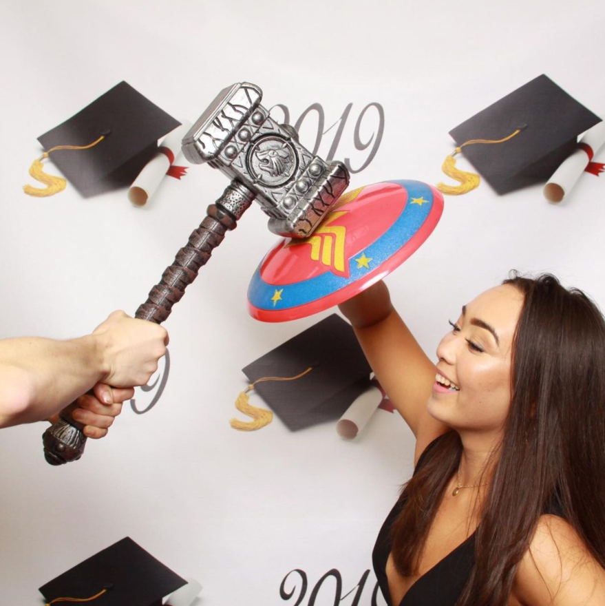 A couple taking a marvel themed picture using wonder woman shield, and thors hammer props