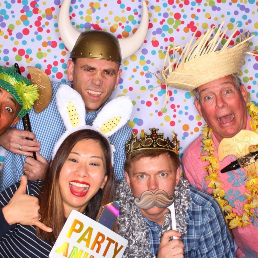 A group of people wearing props taking a photobooth selfie picture in front of a backdrop