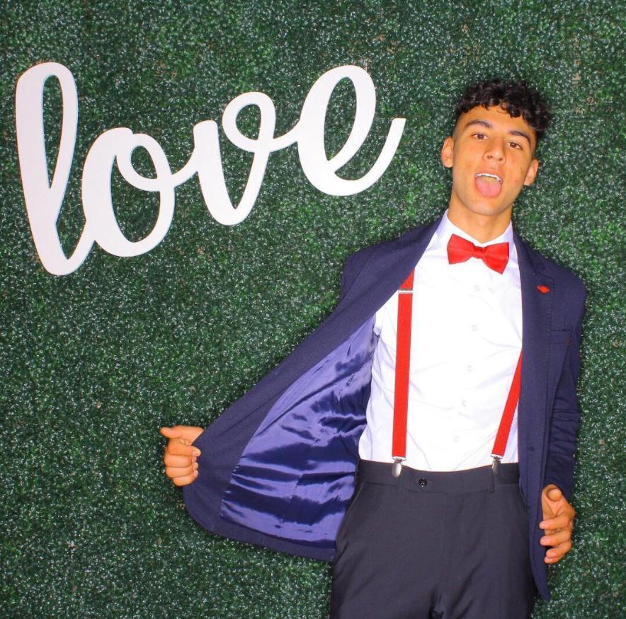 A boy taking his photo in front custom grass backdrop. A custom prop reading 'Love' is also in the frame